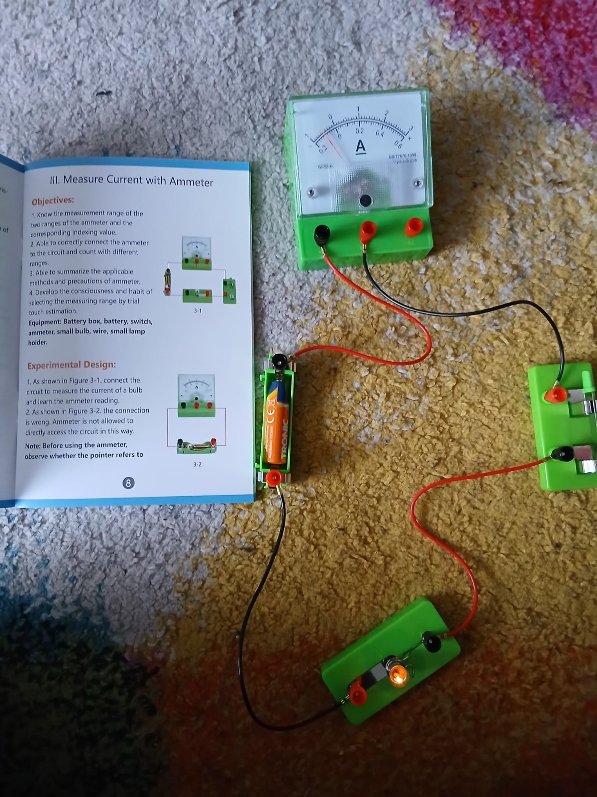 A series circuit with battery, light, switch, and ammeter alongside an instruction book
